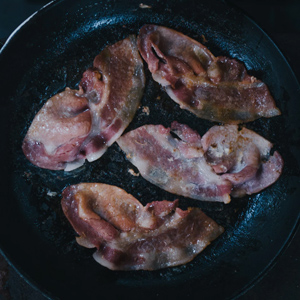 Picture of bacon cooking in a frying pan.